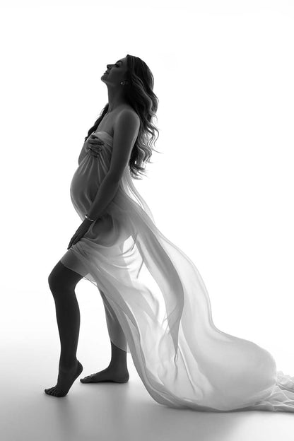 A pregnant woman is posing in a studio. She is holding a chiffon scarf to cover up. The piece of fabric is light and perfect for tossing. 