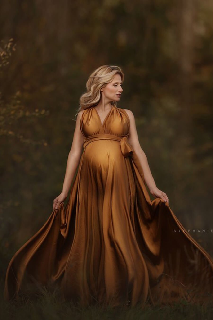 blond pregnant model poses outdoors wearing a long camel dress made of silk. 