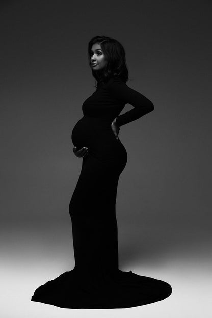 black and white photo of a pregnant model posing in a studio wearing a black long tight dress.