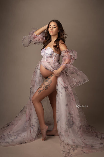 pregnant model poses on her side at a studio wearing a tulle and organza dress with pattern with flowers. the dress is strapless and has attached sleeves made of organza. 