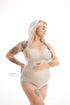 A pregnant woman is wearing a no sleeved bodysuit. She is looking away and holding her belly. She has a lot of tattoo&