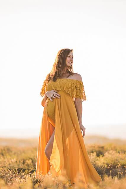 pregnant model poses outside wearing a yellow long dress, off shoulder with a ruffle lace top.