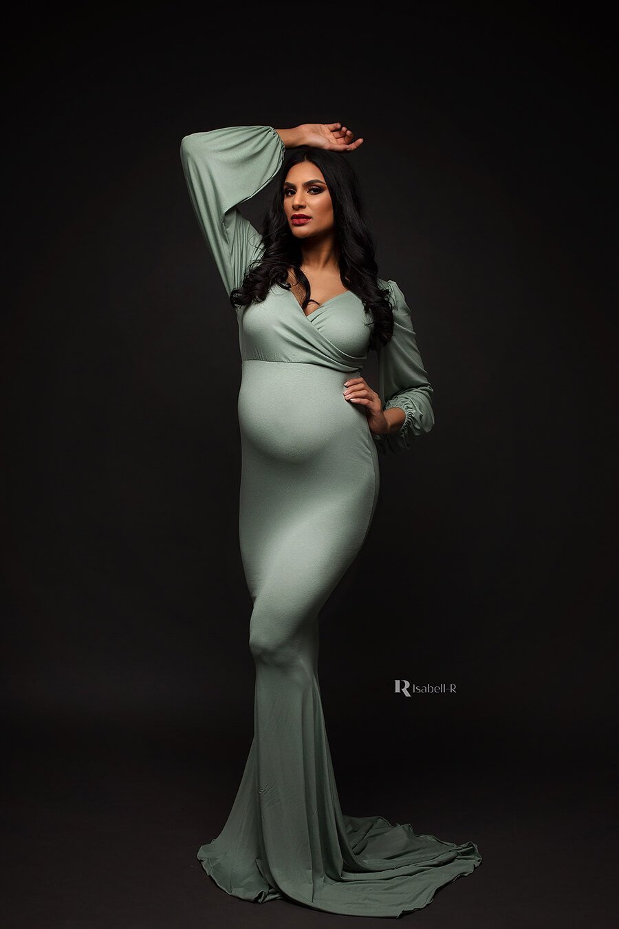brunette pregnant model poses in a dark studio wearing an azur long jersey dress. the dress features an adjustable sweetheart top and bishop sleeves. the dress is long and features a mermaid skirt.
