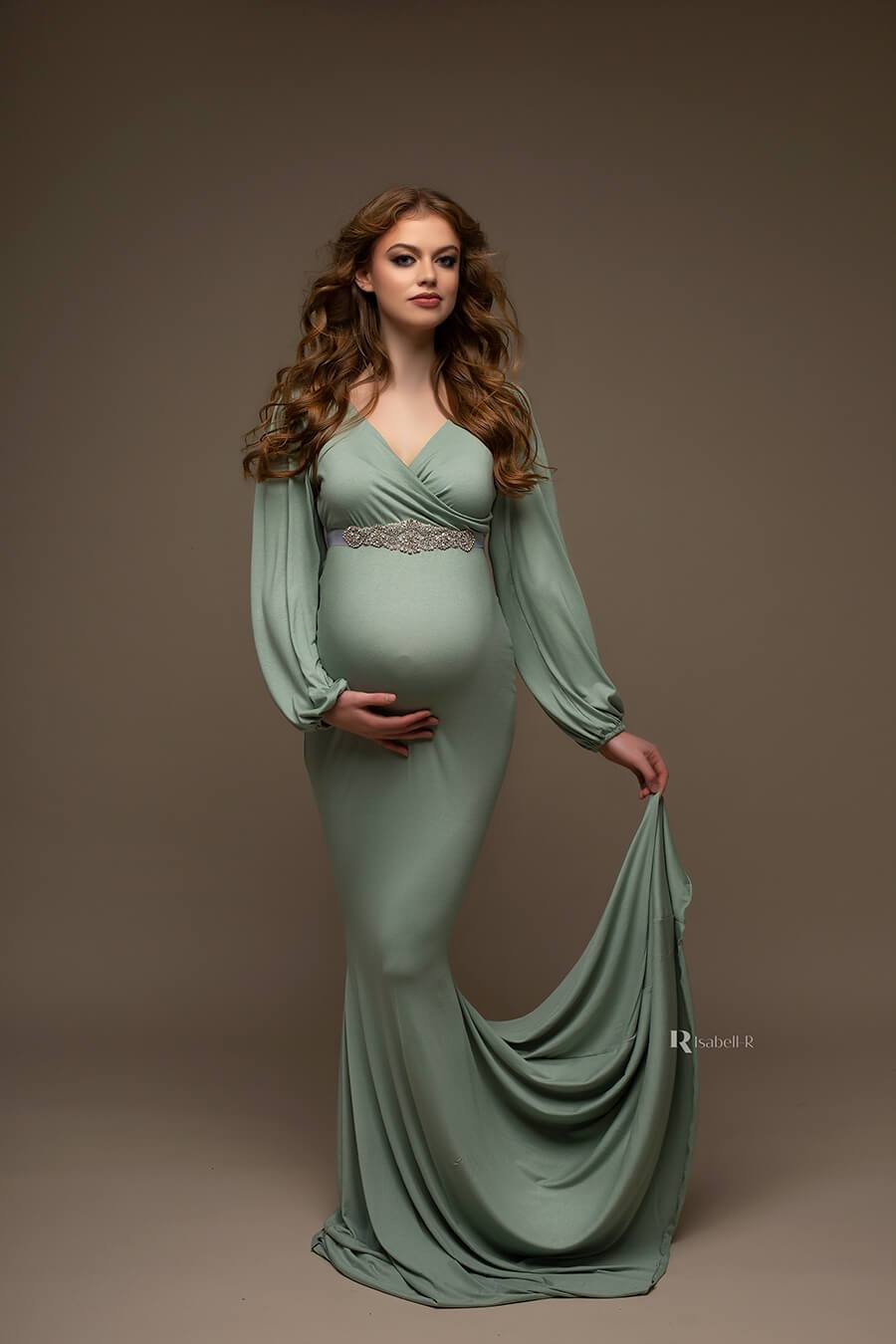 brunette pregnant model poses in a dark studio wearing an azur long jersey dress. the dress features an adjustable sweetheart top and bishop sleeves. the dress is long and features a mermaid skirt.
