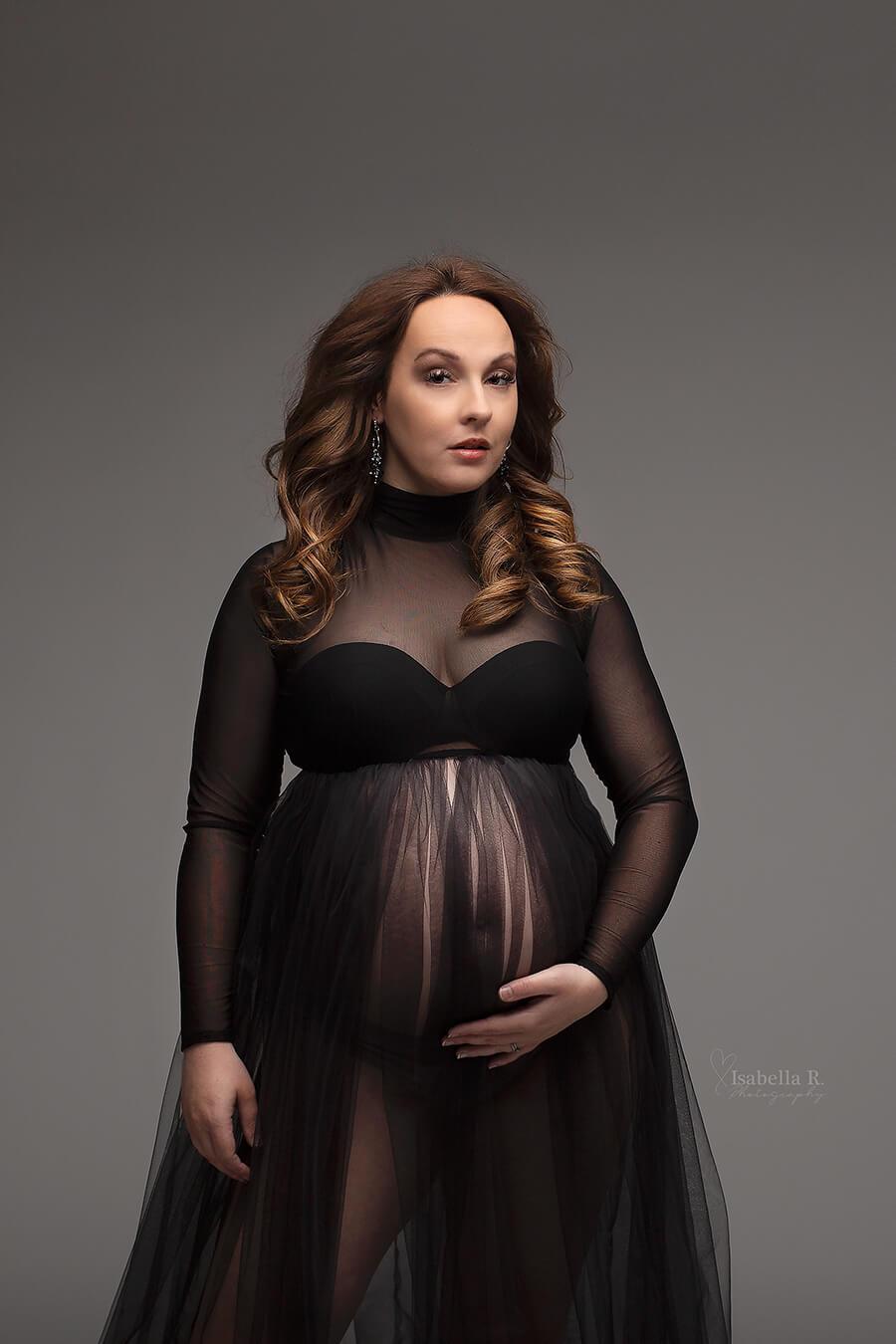 A pregnant woman is wearing a big tulle dress. The dress is see trough and has a turtle neck. It is in the colour black