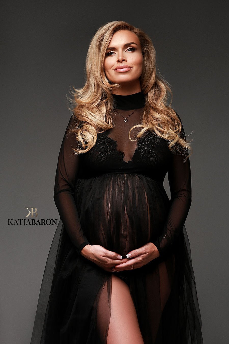 a woman with blonde hair is wearing a black dress. The dress is see trough and made from mesh fabric. The dress has a high turtle neck