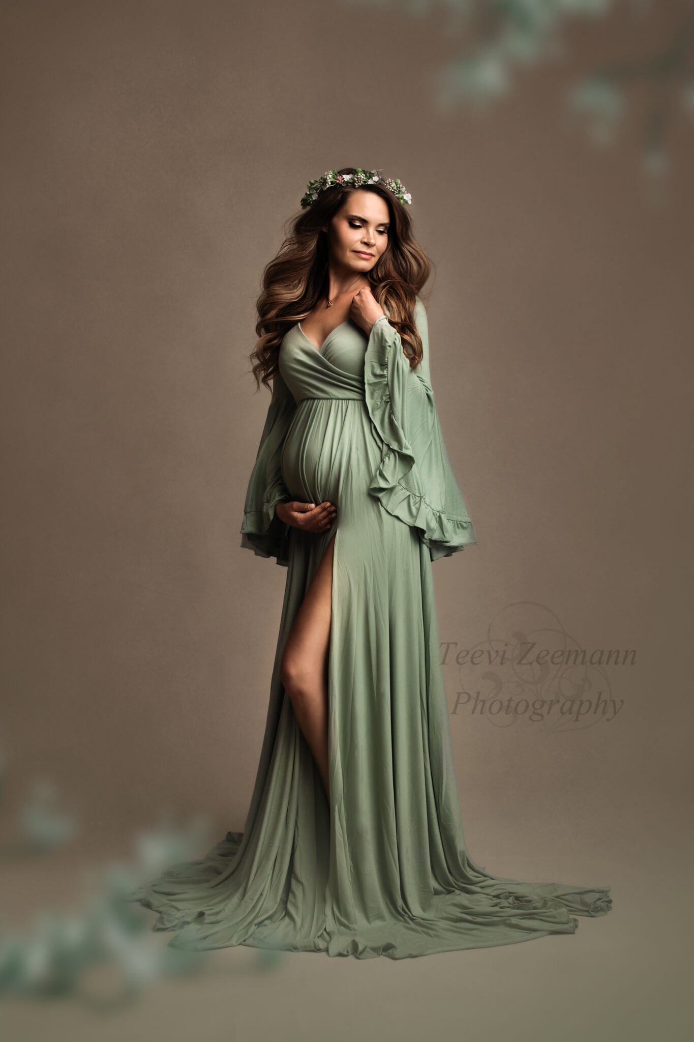 Dark blond pregnant model poses in a studio during a maternity photoshoot wearing a jersey dress designed by Mii-Estilo. The dress features a sweetheart top and bell sleeves. The dress has a split on the side where you can see a bit of the model&