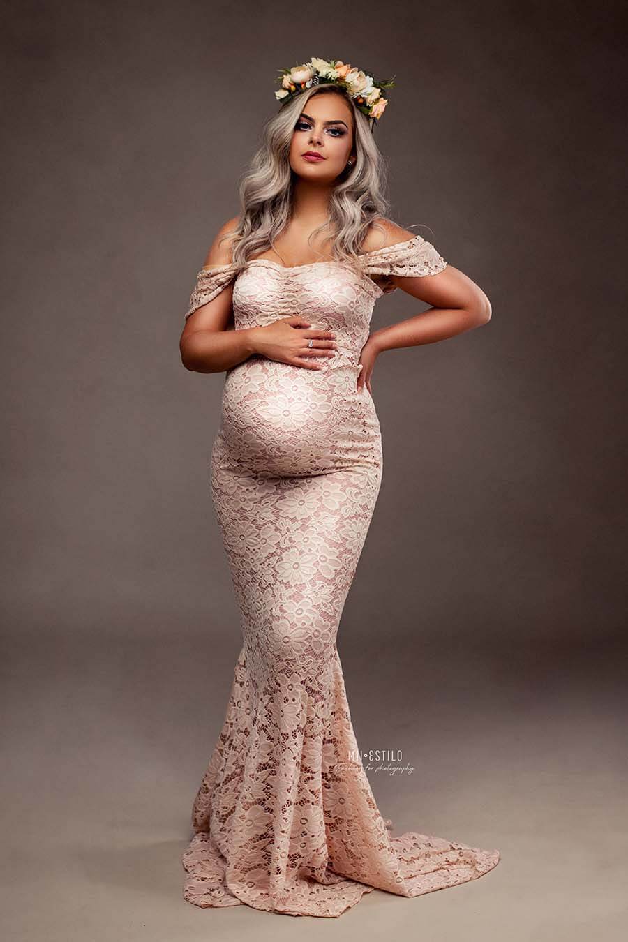 This pregnant woman is wearing a long dusty pink dress. The dress has drop sleeves and is made out of lace. underneath the lace is a jersey layer attached so the dress isn&