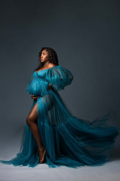 black pregnant model poses in a studio wearing a petrol dress made of jersey and tulle with big puff sleeves