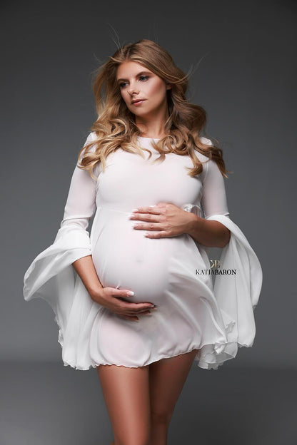 Blonde woman that is pregnant is wearing a short chiffon dress in the colour white