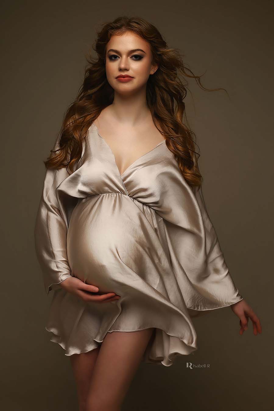 pregnant model poses wearing a sand short dress made of satin. the dress has a low v cut neckline and kaftan style sleeves.