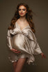 pregnant model poses wearing a sand short dress made of satin. the dress has a low v cut neckline and kaftan style sleeves.