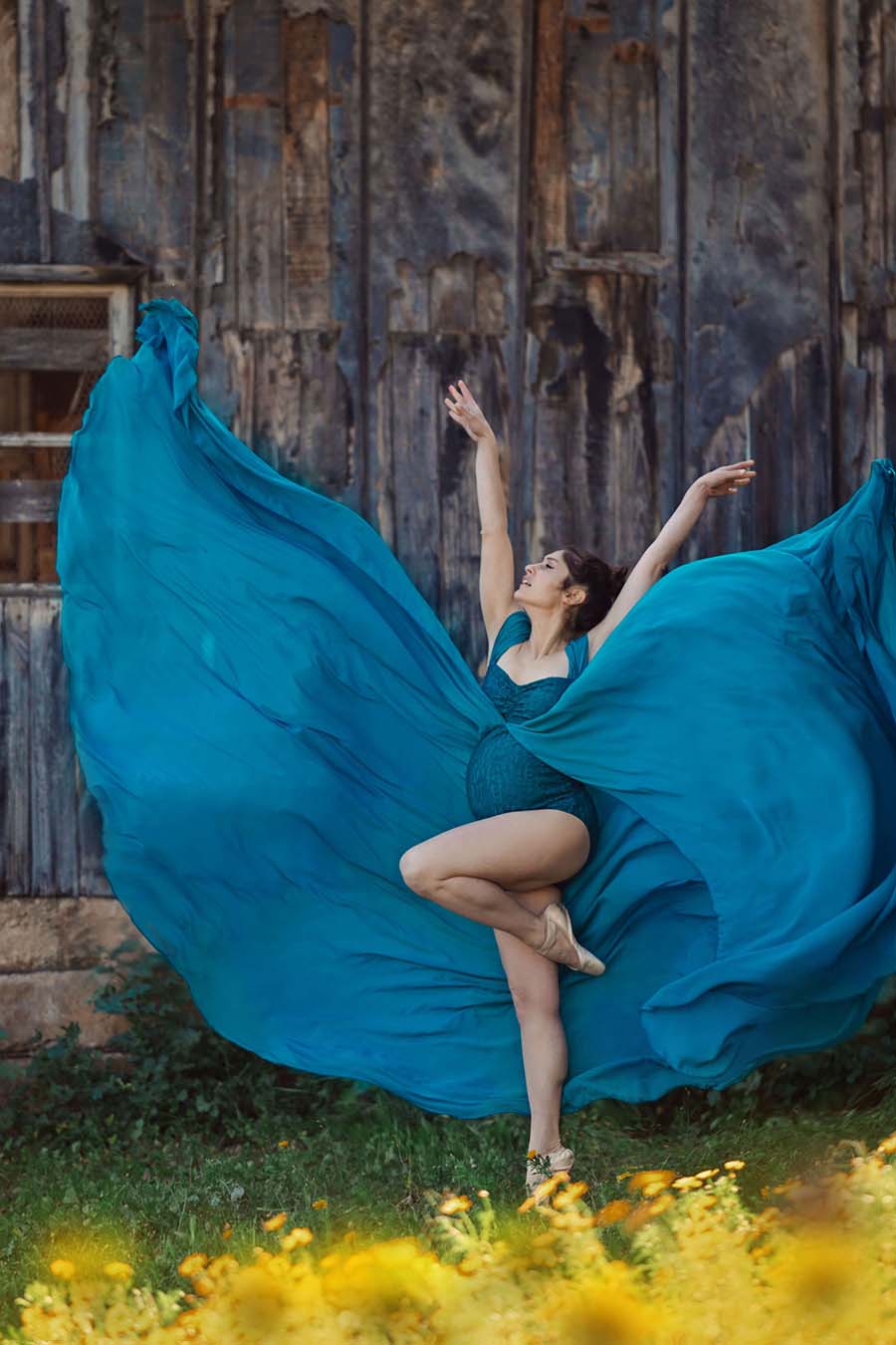 ballerina model poses outdoor wearing a long petrol dress with a chiffon train and a lace bodysuit. 