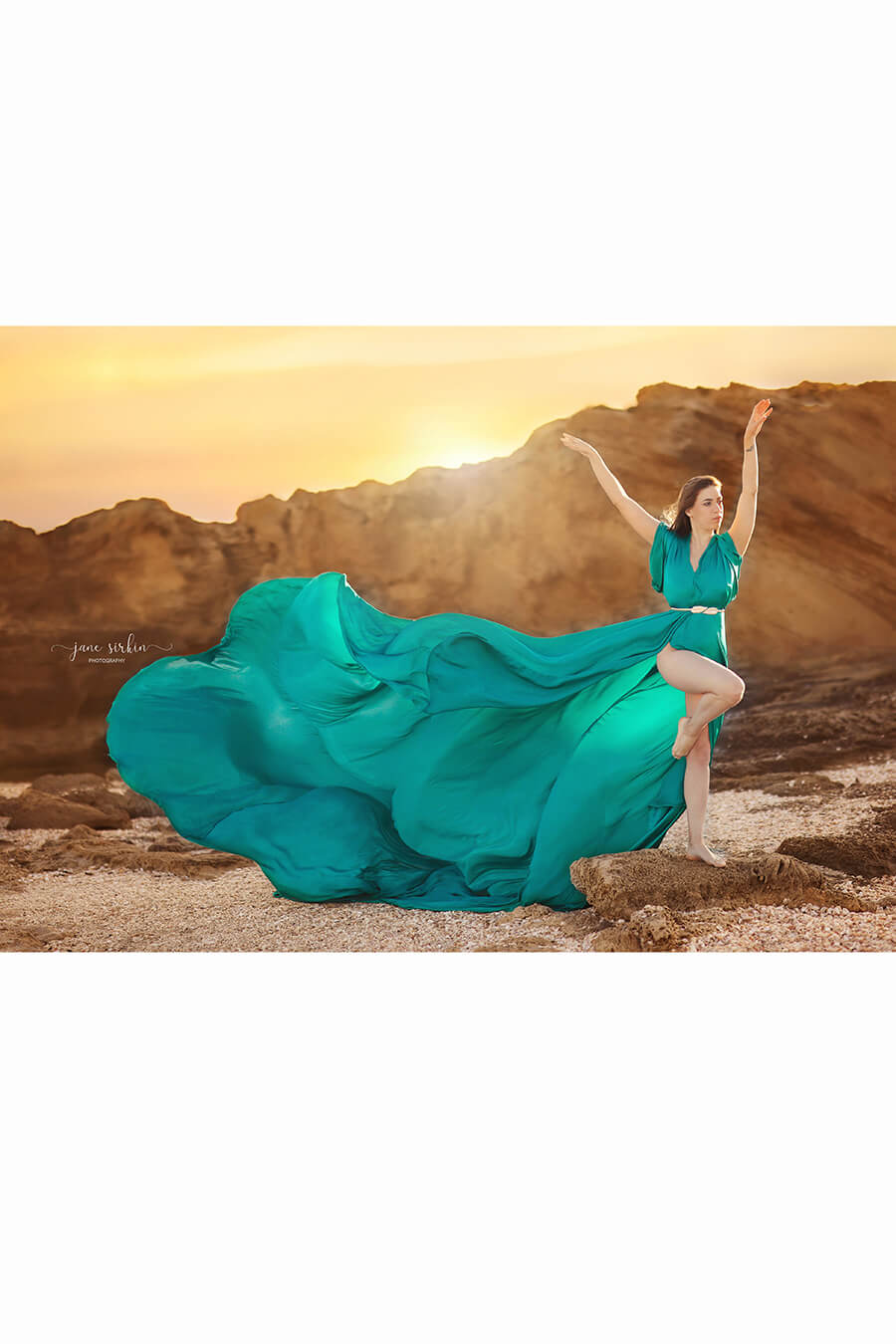 brunette model poses outdoors at a rocky place wearing a emerald silky dress with extra long train to create flying movements.