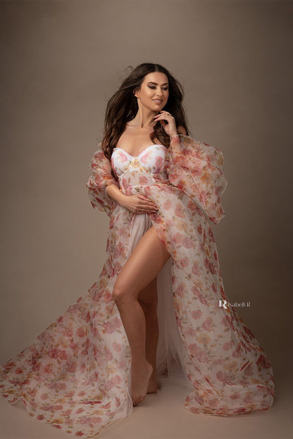 brunette model smiles during her glamour photoshoot. she is wearing a flower patterned dress made of tulle and organza. one of her legs can be seen through the split from the dress.