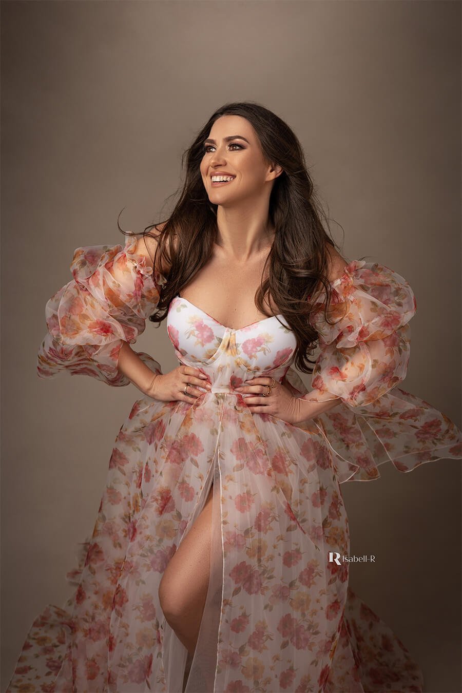 brunette model smiles during her glamour photoshoot. she is wearing a flower patterned dress made of tulle and organza.