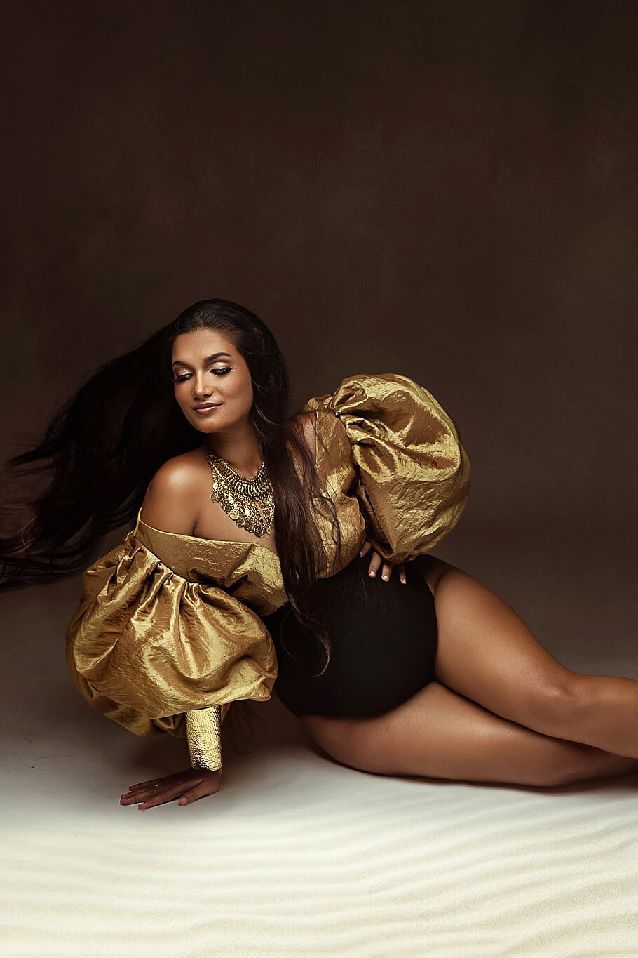 dark haired pregnant model poses in a studio wearing a bodysuit in two colors. the top is made of golden taft and the bodice of black jersey. the top has exaggerated puff sleeves.