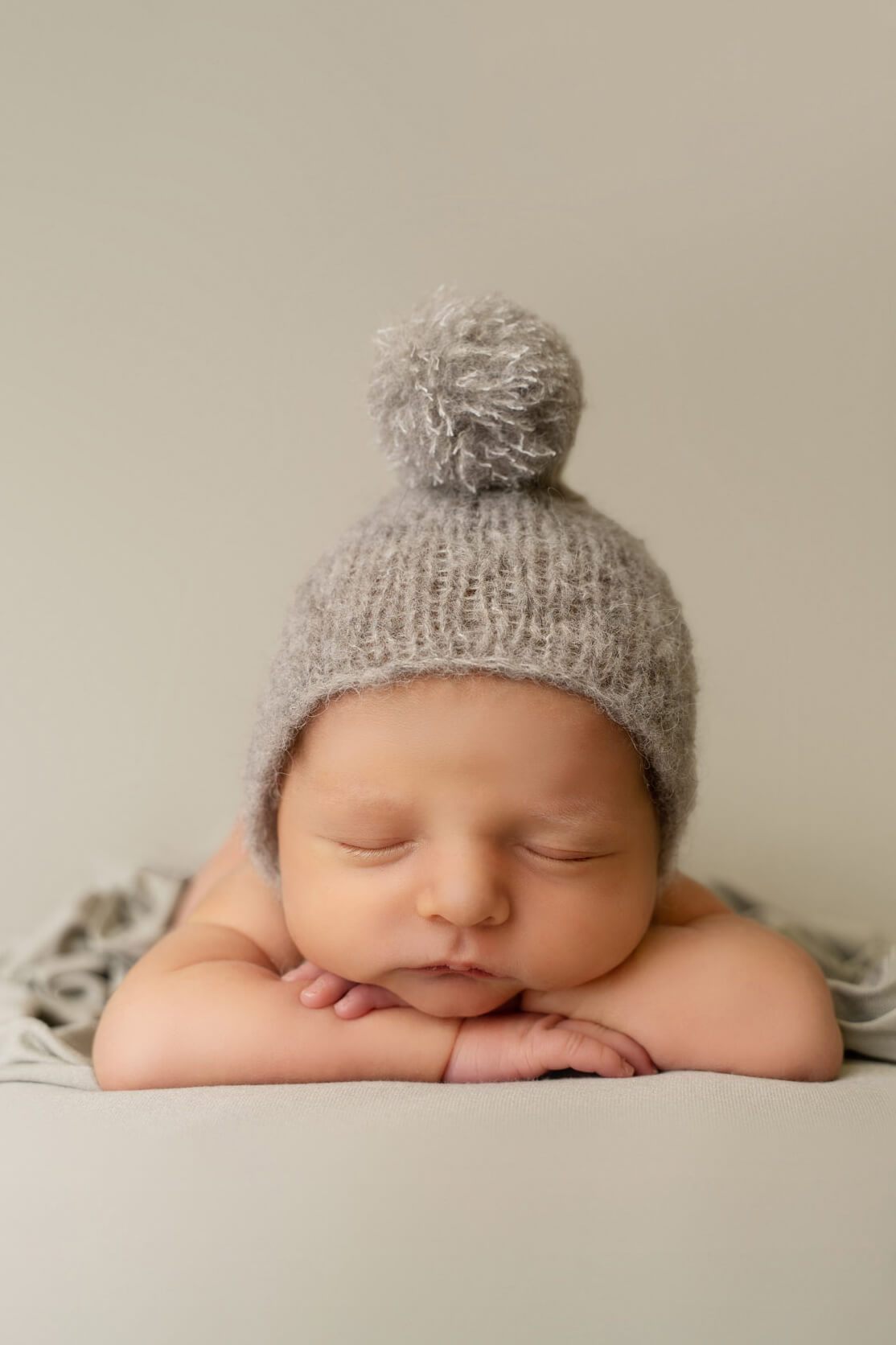 A baby is laying on a khaki green blanket. She has also a little knitted cap on her head