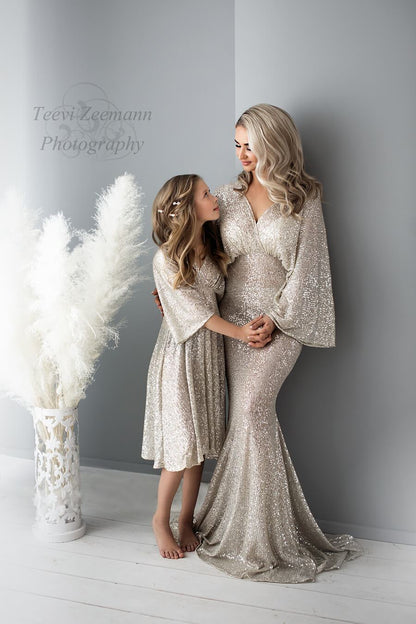 model poses together with her daughter on a studio wearing a long glitter dress.  