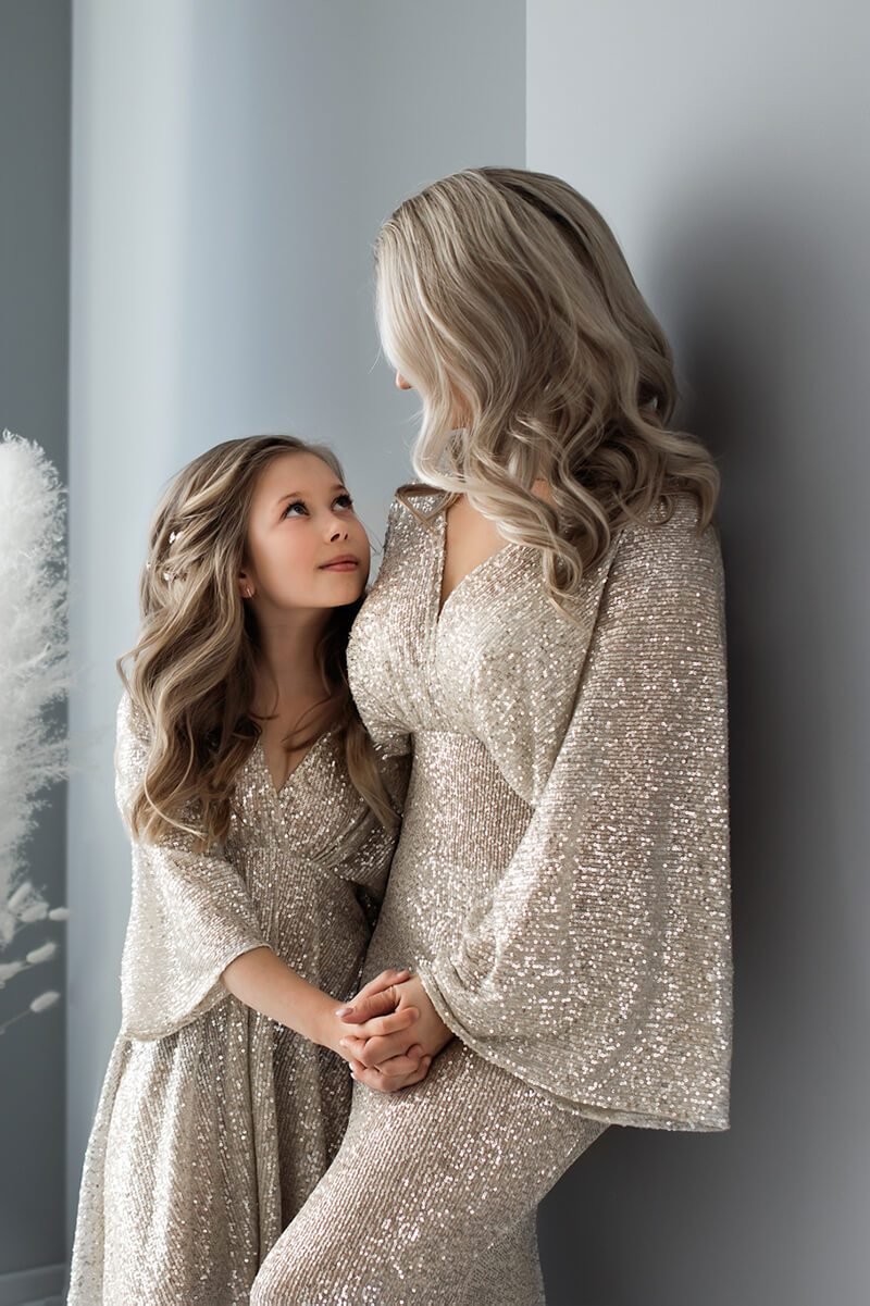 mother and daughter pose together in a studio wearing a long glitter dress.