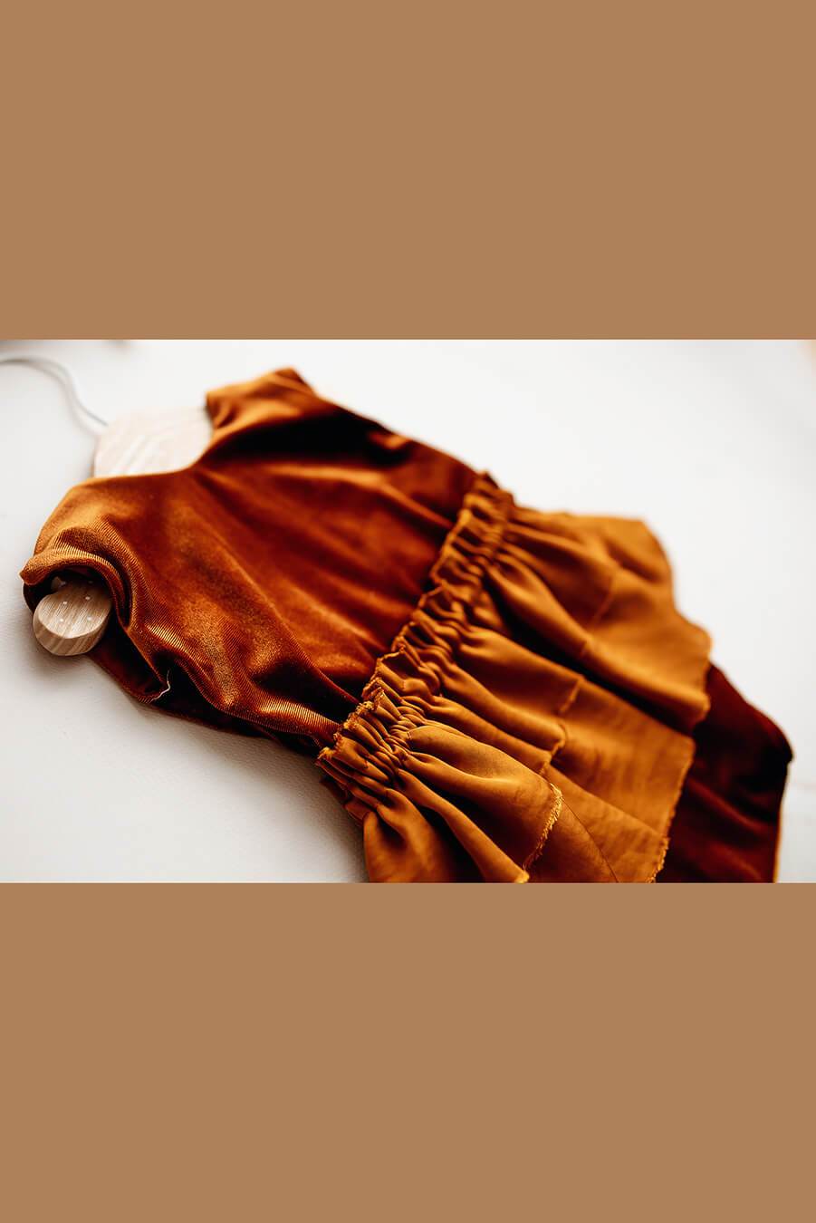 A baby romper in the colour cognac. The romper is made from velour. It also has a skirt