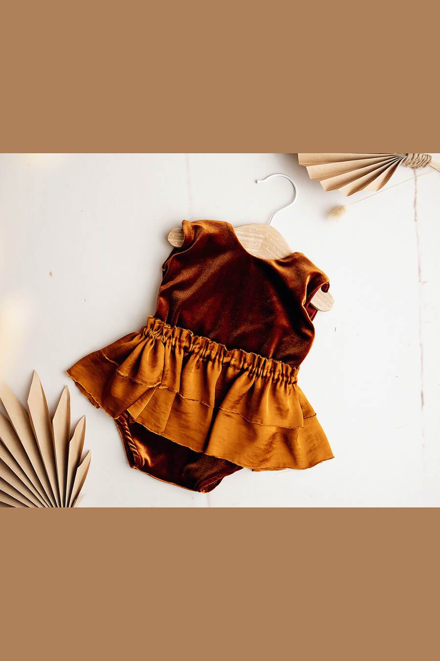 A little girls romper is laying on the ground. The romper is velour with a little skirt over it. The background is white