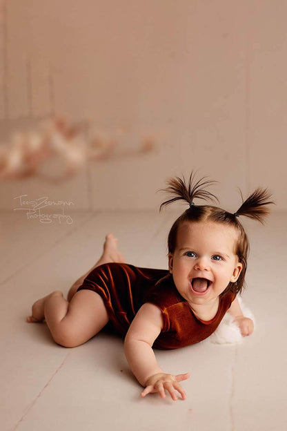 A little baby girl is laying on the ground. She has two ponytails in her hair. She is wearing a velour romper