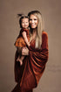 A woman is holding her little girl. The little girl is wearing a cognac romper with a skirt. The mother is wearing a long velour dress in cognac