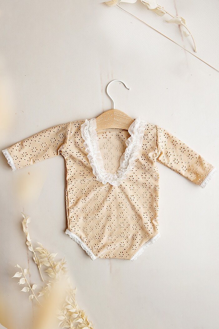 This is a product picture of our Myrthe Newborn Romper Sand. The romper is made of Embrodery Lace and has long sleeves with high round neckline. The sleeves and the opening for the legs are finished with lace. The back of this romper has a lower round line and is finished with lace.