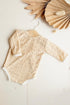 This is a product picture of our Myrthe Newborn Romper Sand. The romper is made of Embrodery Lace and has long sleeves with high round neckline. The sleeves and the opening for the legs are finished with lace. In the corner of this picture you can see flowers for decoration.