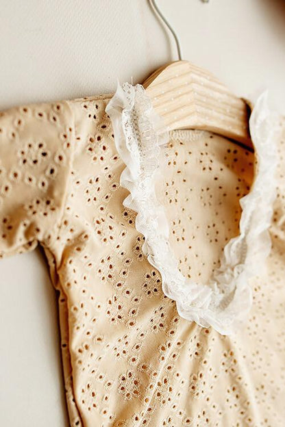 This is a product picture of our Myrthe Newborn Romper Sand. The romper is made of Embrodery Lace and has long sleeves with high round neckline. The sleeves and the opening for the legs are finished with lace. The back of this romper has a lower round line and is finished with lace.