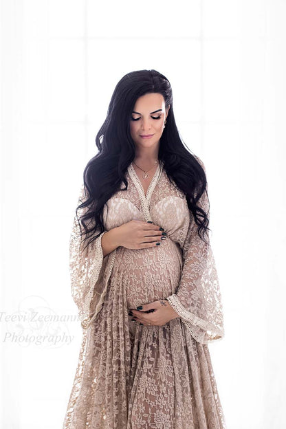 pregnant model with long dark hair faces down while holding her bump with both hands. she has her eyes closed and is wearing a sand colored dress made of lace with special brodery details on the endings.