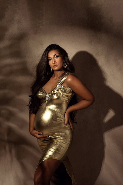 dark haired model poses in a studio wearing a long tight golden lamee dress with a side split.