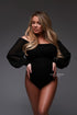 A pregnant woman is wearing a black bodysuit. She has long blonde hair and is looking to the side. She has long beige colored nails