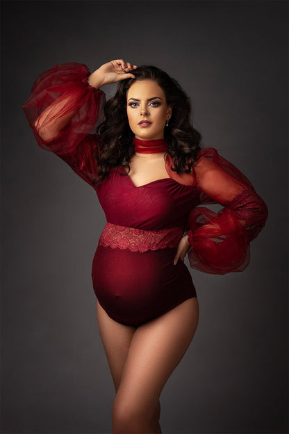 pregnant brunette model poses in a studio wearing a bordeaux red bodysuit with long bishop tulle sleeves with lace details. 