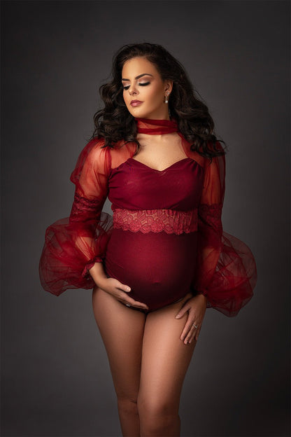 pregnant brunette model poses in a studio wearing a bordeaux red bodysuit with long bishop tulle sleeves with lace details.