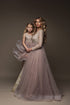 omother and daughter pose together in a studio wearing matching outfits made of lace and tulle. the mom has a long sleeves top in lace while the kids has a taktop style. both skirts are made of matching sand tulle. they are both looking straight to the camera.