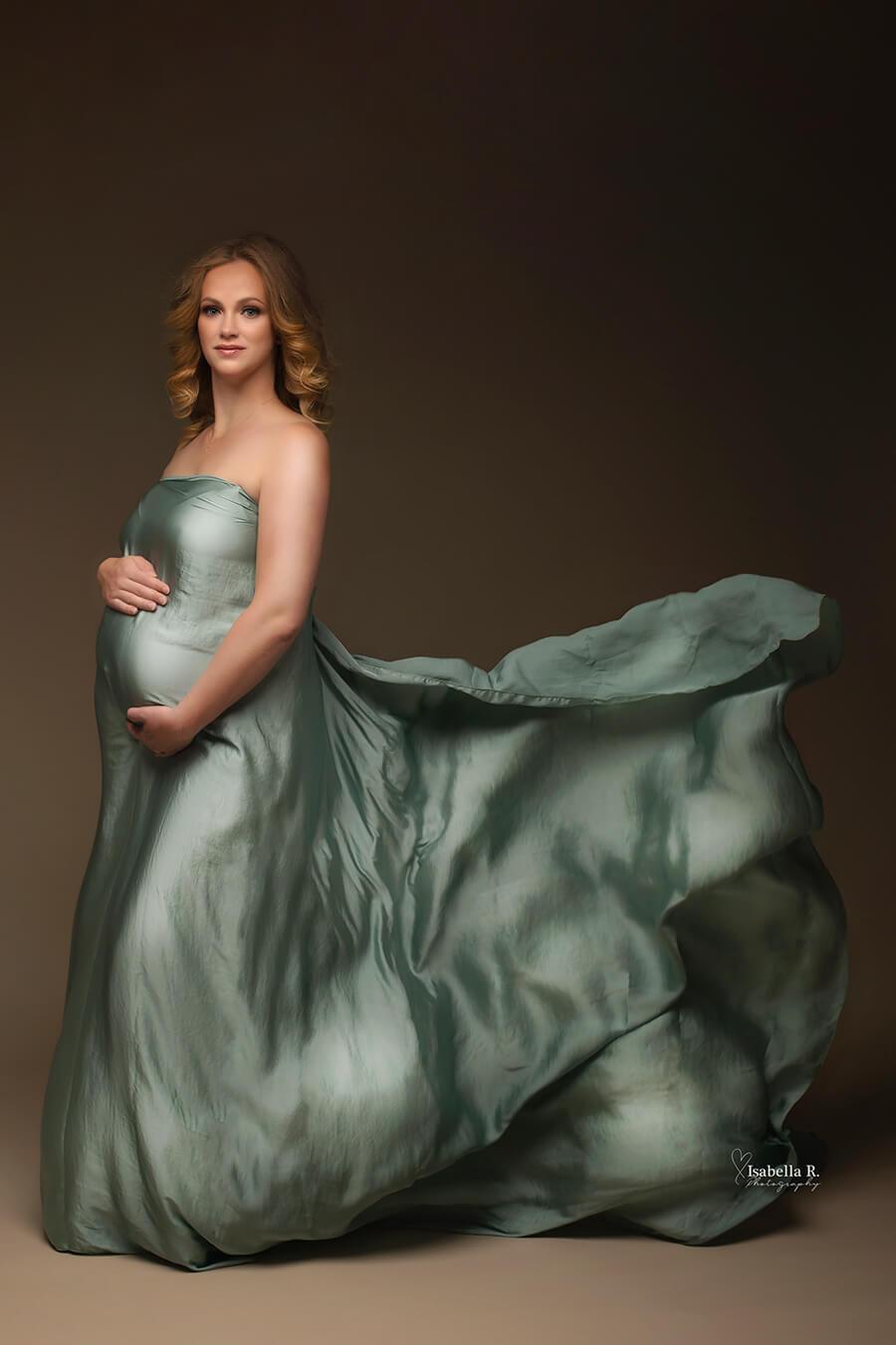 A maternity photo of a pregnant woman that is wearing a scarf as a dress. The piece at the end of the scarf is thrown to create a wave effect