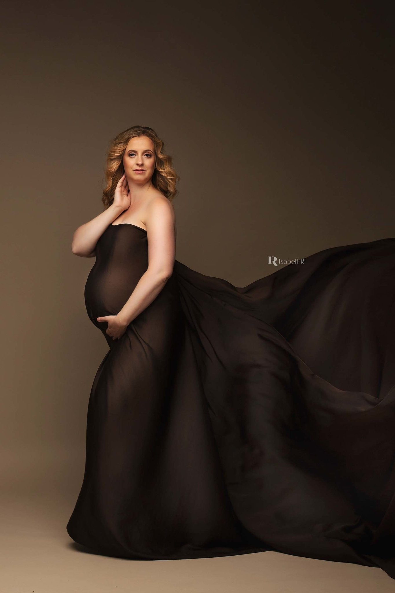 A pregnant woman is wearing a scarf as a dress. The scarf is in the colour brown. She has short blonde hair