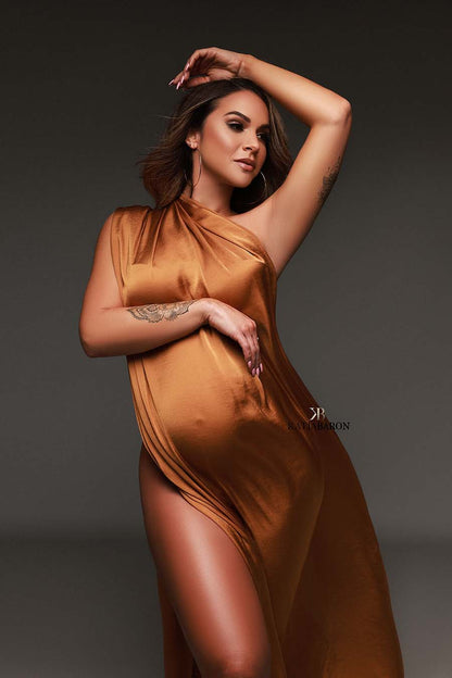 Pregnant model poses in a studio wearing a cognac camel scarf. One of her arms is up while the other rests on her bump. 