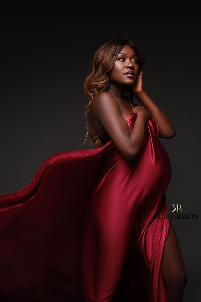A pregnant woman is posing in a studio. the windmachine is blowing the scarf around the model. She is wearing the silky scarf cherry. The fabric has a wave effect because of the wind.