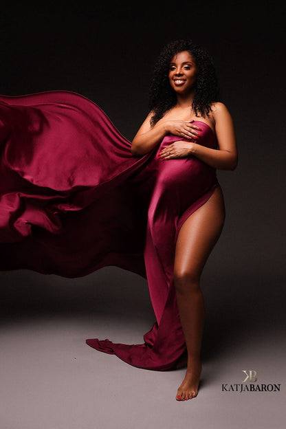 A pregnant model is posing for the camera. They have wrapped the silky scarf around her. Her leg is sticking out of the fabric. The fabric is being tossed in the air.