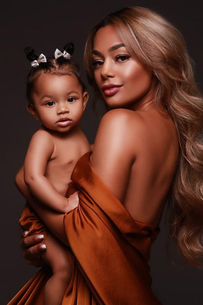 mother poses together with her baby girl wearing a cognac scarf wrapped around her arms and staring at the camera.