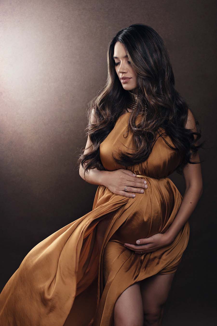 pregnant woman poses for a close up wearing a silky scarf. she has a golden necklace to match the style. 