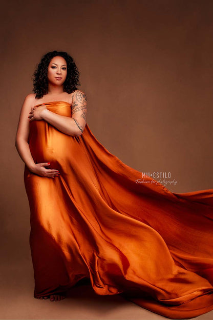 pregnant model poses in a studio covering her body with a cognac colored scarf. she stares at the camera while holding her bump.