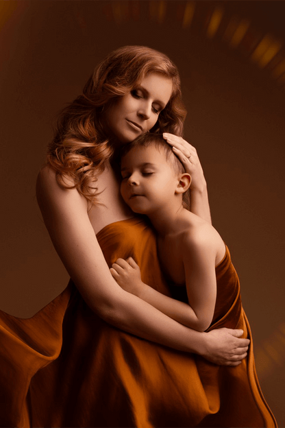 mother and kid are holding each other and they are both wrapped in a cognac silky scarf
