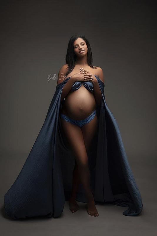model poses in a studio wearing a denim piece of fabric covering her breasts, her belly and legs are uncovered and her eyes are closed. 