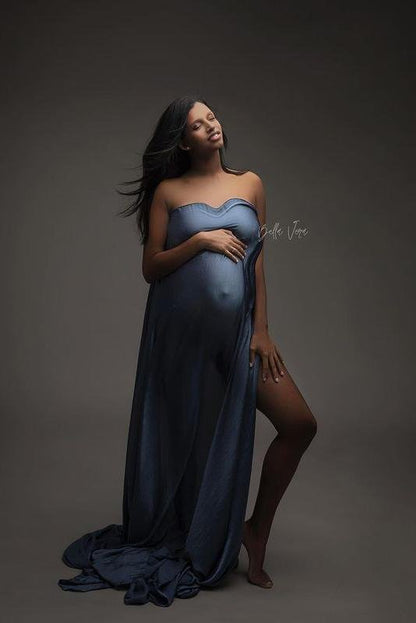 pregnant model poses in a studio wearing a piece of denim draping fabric covering her breast, belly and leg. she is facing up and has her eyes closed. 