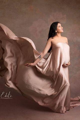 This is a photograph of a pregnant woman. She is modeling with a silky scarf as dress. The fabric is being tossed in the air and slowly falling down. She is smiling and looking up.