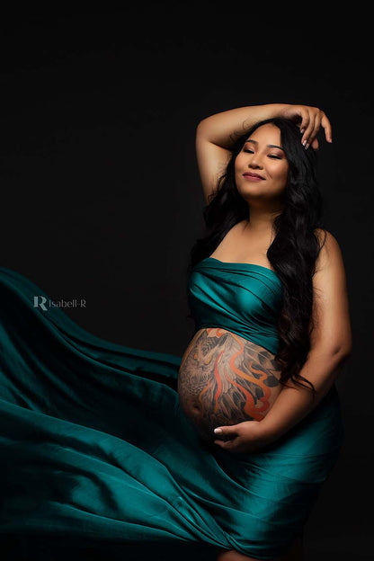 A pregnant woman is wrapped in the silky scarf azur. You can see her belly. She has a huge owl tattoo on her belly. She is posing with one hand on her head and the other hand is underneath her belly. She has long black hair.